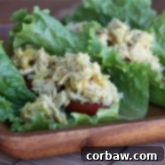 A top-down view of a single lettuce wrap filled with tangy tuna salad, garnished with sliced tomatoes, presented on a rustic wooden plate.