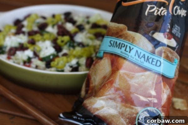 Close-up of a vibrant Layered Greek Hummus Dip with a spoon, ready to be served with crunchy pita chips.