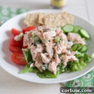 A serving of creamy salmon salad on a bed of fresh greens with crackers on the side.