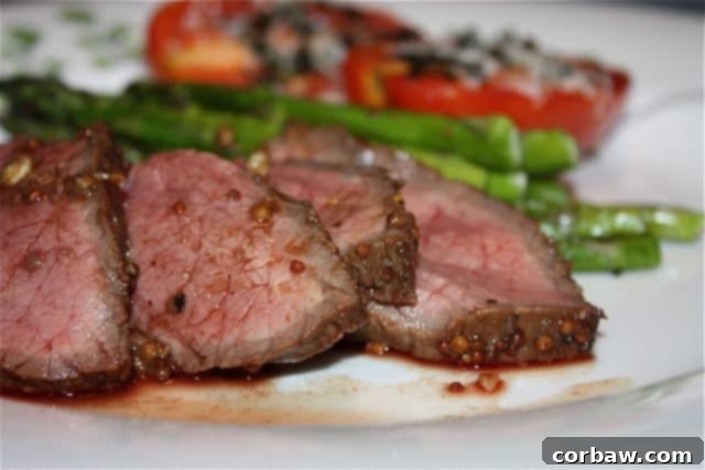 sliced london broil on white plate with asparagus and tomatoes in background