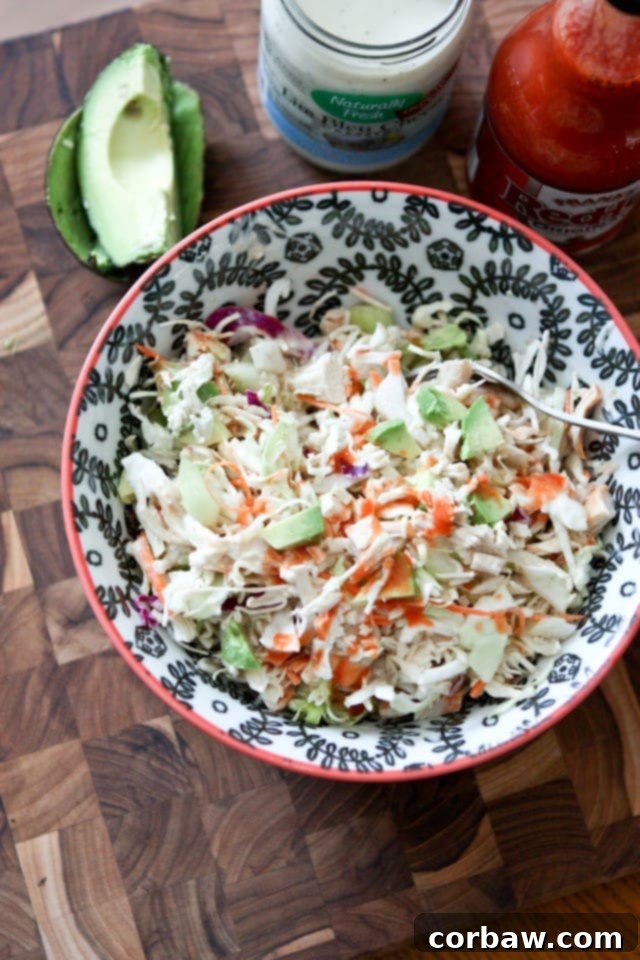 top view of bowl of chicken slaw salad topped with buffalo sauce with a container of blue cheese and buffalo hot sauce and half of an avocado