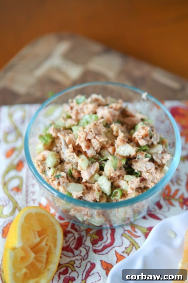 Glass bowl filled with freshly prepared blackened salmon salad, garnished with a vibrant lemon half, placed on a woven placemat, ready to be served.