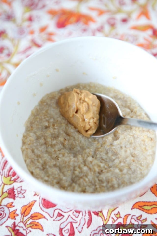 A hand stirring warm peanut butter into a bowl of oats and mashed banana, showcasing the simple and easy preparation of this nutritious meal