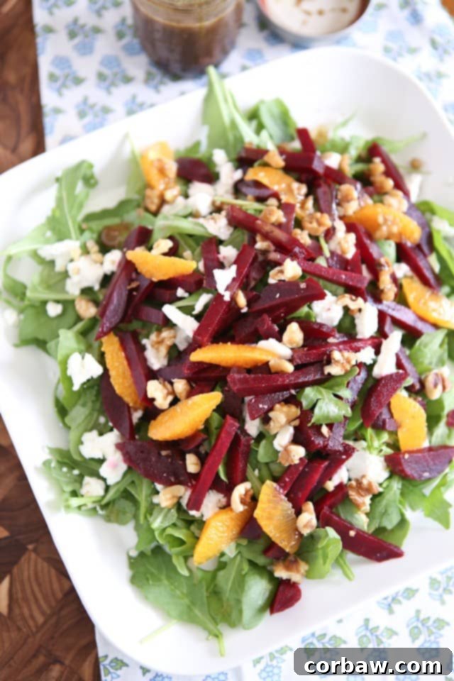 plate of arugula salad topped with goat cheese, beet strips, orange slices, and walnuts