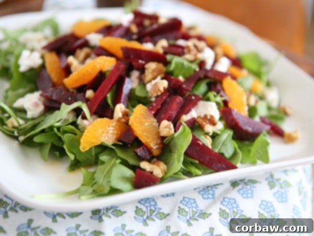 plate of arugula salad topped with goat cheese, beet strips, orange slices, and walnuts