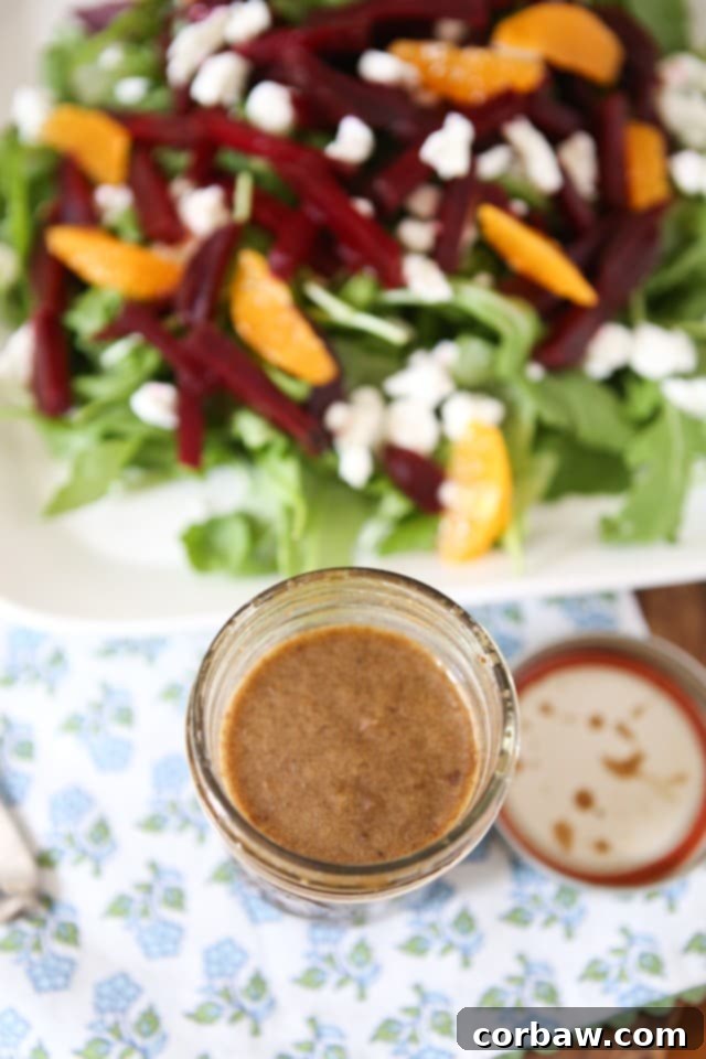 mason jar of dressing next to plate of arugula salad topped with goat cheese, beet strips, orange slices, and walnuts
