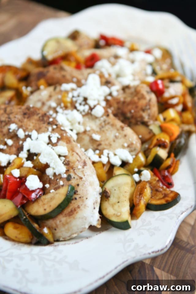 Close-up of a plate featuring balsamic-glazed chicken, sweet peppers, and zucchini, elegantly topped with crumbled feta cheese.