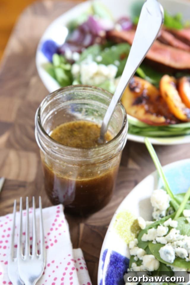A charming jelly jar filled with golden honey balsamic dressing, with a fresh green salad blurred in the background, signaling health and homemade goodness.